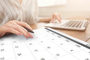 Business Scheduling. Unrecognizable Woman Working On Laptop And Checking Calendar At Workplace